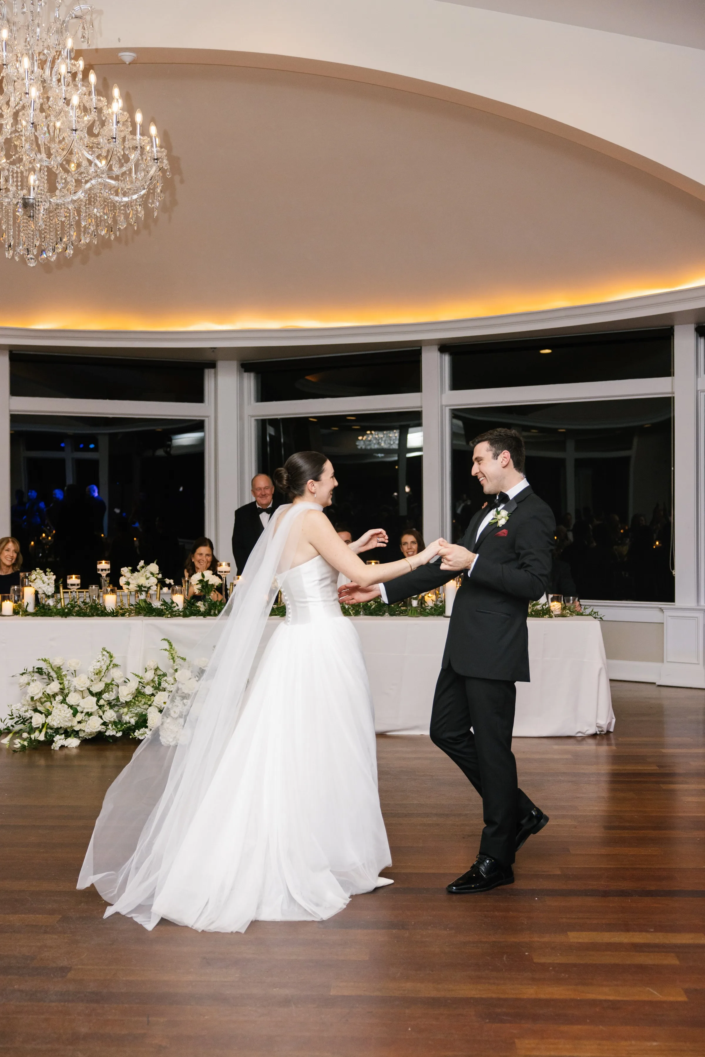 Bride and groom share their first dance at an elegant Newport RI wedding reception venue with crystal chandelier and white floral arrangements, performed live by Soul City Band