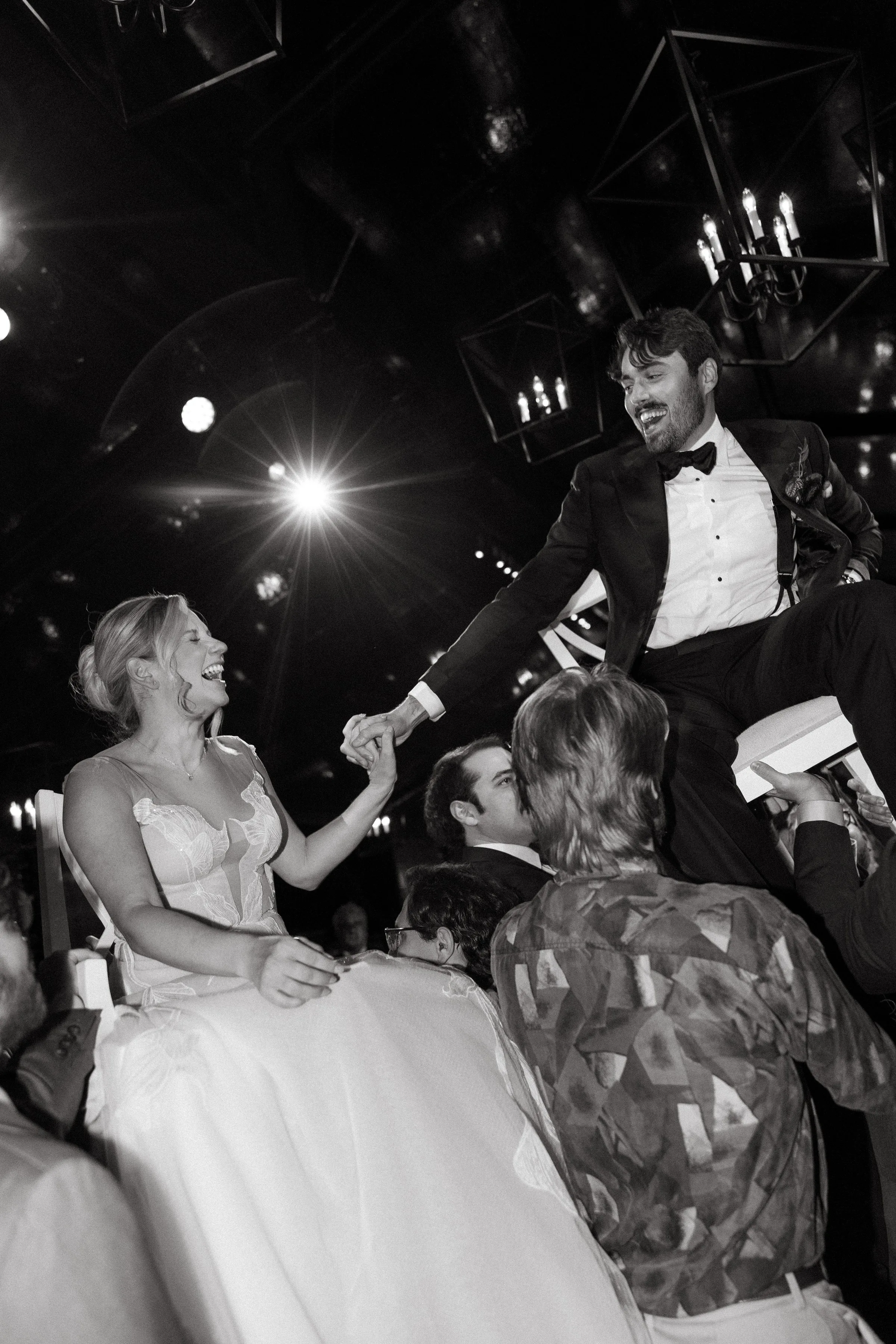 Bride and groom laughing while being lifted in chairs during the hora at a lively wedding reception featuring Soul City Band in Newport RI