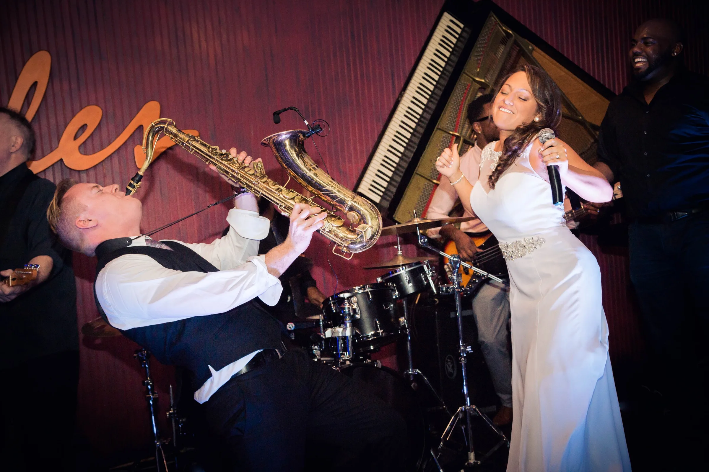 Soul City Band saxophonist and vocalist performing energetically on stage at a live wedding reception in Newport RI with drums and grand piano in the background
