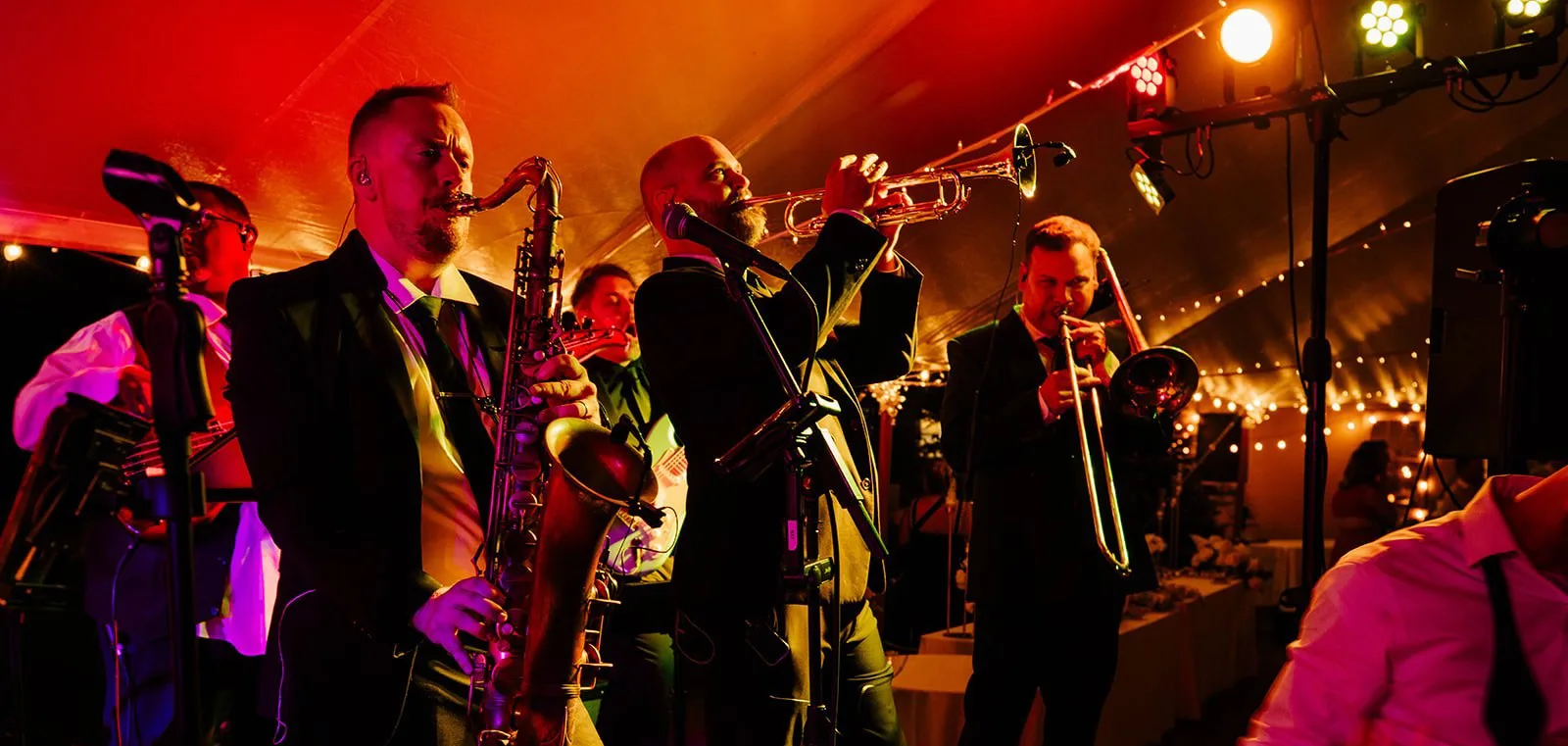 Soul City Band horn section featuring saxophone trumpet and trombone players performing live at a tented wedding reception with warm festive lighting in Newport RI