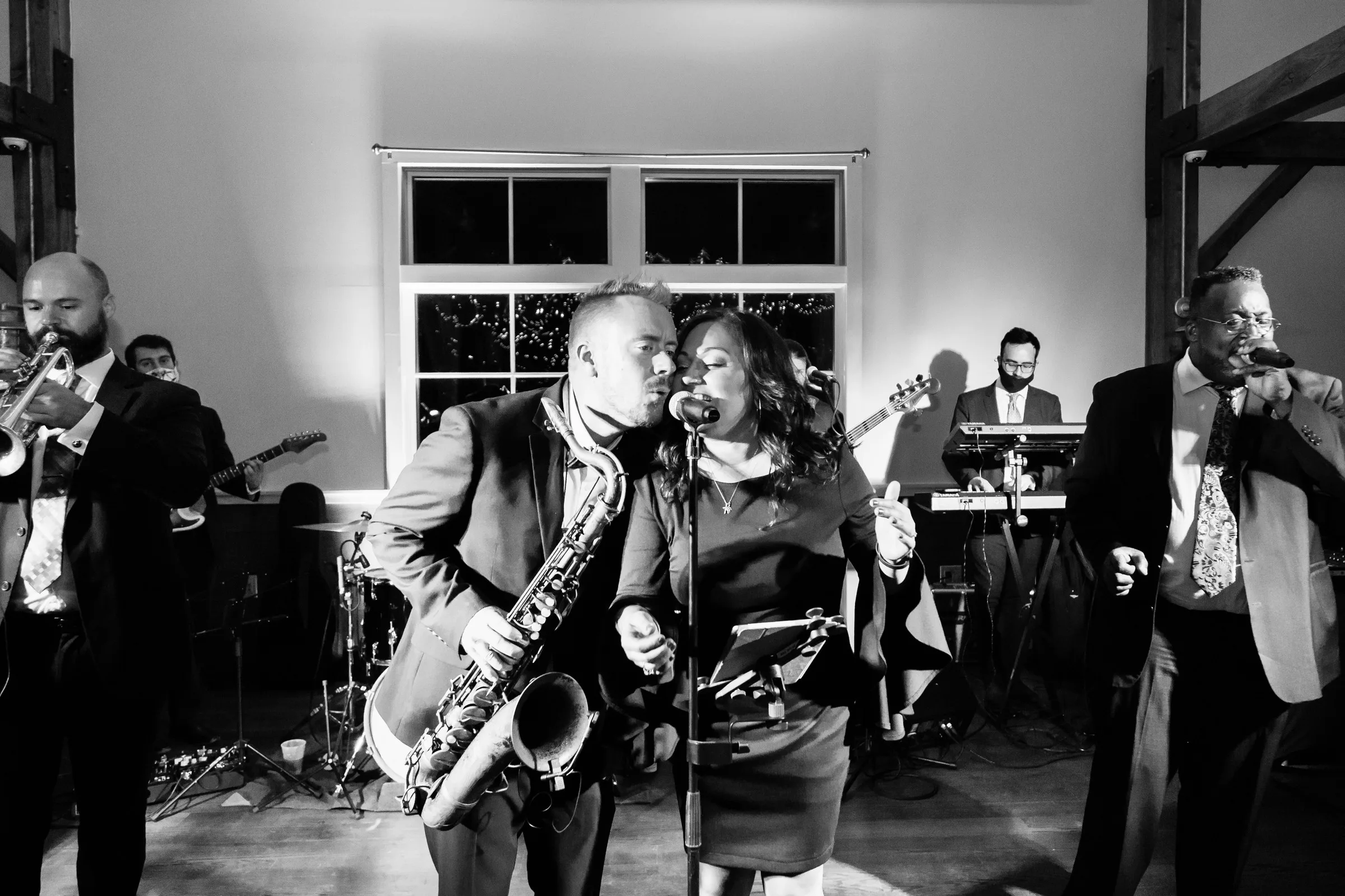 Soul City Band saxophonist and female vocalist performing live at an indoor wedding reception in Newport RI with full band including brass guitarist and keyboardist in background