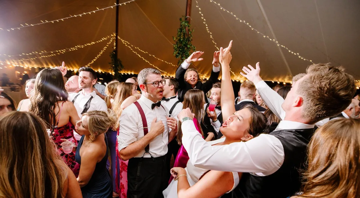 Energetic wedding reception dance floor packed with guests dancing and celebrating under string lights at a tented venue, featuring live entertainment by Soul City Band in Newport RI and Boston MA